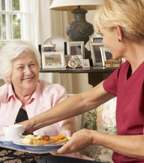 caregiver preparing meal for old woman